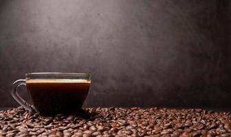 The side view of a coffee cup and group of black coffee beans is the background. Strong black espresso, Grounds of coffee background, texture photo