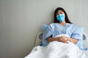 triste asiático paciente mujer acostado en el hospital cama y vistiendo un cara máscara a proteger coronavirus. concepto de salud cuidado, cuarentena coronavirus covid-19 y salud seguro. foto