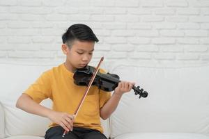 un pequeño niño asiático tocando y practicando violín instrumento de cuerda musical en casa, concepto de educación musical, inspiración, estudiante de escuela de arte adolescente. foto