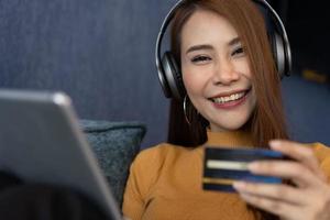 Portrait of young woman wear headphones and holding tablet and banking credit card, transferring money online, shopping goods in internet store, purchasing services, satisfied with secure payments. photo