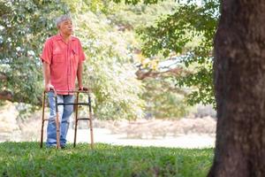contento antiguo mayor asiático hombre usos un caminante y camina en el parque. concepto de contento Jubilación con cuidado desde un cuidador y ahorros y mayor salud seguro foto