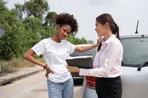 Women drivers Talk to Insurance Agent for examining damaged car and customer checks on the report claim form after an accident. Concept of insurance, advice auto repair shop and car traffic accidents. photo