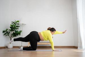 Asian overweight woman doing stretching exercise at home on fitness mat. Home activity training, online fitness class. Stretching training workout on yoga mat at home for good health and body shape. photo