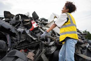 Mechanical woman owner small business inspecting standing in the car junkyard, Dirty male repairman choosing spare parts on car junkyard, Used of vehicle part for recycling in the scrap yard garage. photo