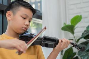 A Little Asian kid playing and practice violin musical string instrument against in home, Concept of Musical education, Inspiration, Teenager art school student. photo