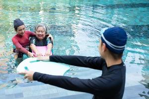 Young trainer helping senior woman in aqua aerobics and working out in the pool. old woman and mature man doing aqua aerobics exercise in swimming pool, Elderly sports, and active lifestyle concept.