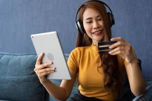 Portrait of young woman wear headphones and holding tablet and banking credit card, transferring money online, shopping goods in internet store, purchasing services, satisfied with secure payments. photo