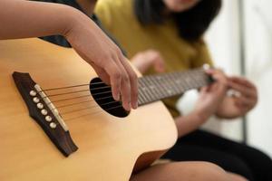 Asian boy playing guitar with mom in the living room for teaching him son play guitar, feel appreciated and encouraged. Concept of a happy family, learning and fun lifestyle, love family ties photo