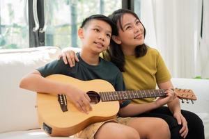 la madre asiática abraza al hijo, el niño asiático tocando la guitarra y la madre se abrazan en el sofá y se sienten apreciados y alentados. concepto de una familia feliz, aprendizaje y estilo de vida divertido, amar los lazos familiares foto