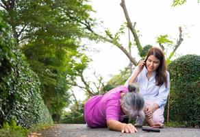 Asian senior woman fell down on lying floor because faint and limb weakness and pain from accident and woman came to help support and call emergency. Concept of old elderly insurance and health care photo