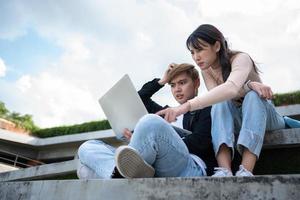 Asian students sitting on steps and use computer laptops to discuss before exams, Student lifestyle at university. Group of student do a project together photo