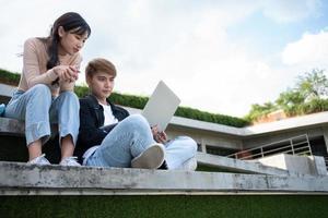 Asian students sitting on steps and use computer laptops to discuss before exams, Student lifestyle at university. Group of student do a project together photo