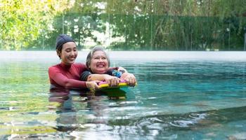 Young trainer helping senior woman in aqua aerobics and working out in the pool. old woman and mature man doing aqua aerobics exercise in swimming pool, Elderly sports, and active lifestyle concept. photo