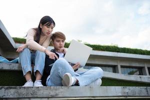 Asian students sitting on steps and use computer laptops to discuss before exams, Student lifestyle at university. Group of student do a project together photo