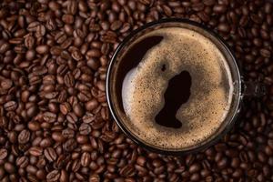 The top view of a coffee cup and group of black coffee beans is the background. Strong black espresso, Grounds of coffee background, texture photo