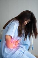 Unhappy Asian patient woman sitting on the hospital bed and holding on stomach suffering. Abdominal pain that comes from menstruation, diarrhea, or indigestion. Sickness and healthcare concept photo