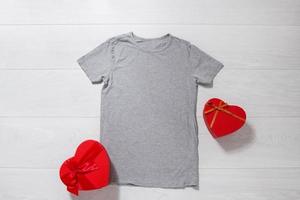 Grey tshirt mockup. Valentines Day concept shirt, gift boxes heart shape on wooden background. Copy space, template blank front view t-shirt clothes. Romantic outfit. Flat lay holiday fashion photo