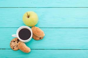 Cup of coffee with croissants and cookies and red roses on blue wooden background. Copy space. Mock up. Top view. Valentine mother day. photo