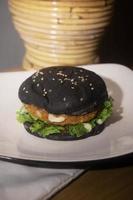 Close up photo of the opened black burger on a white plate is highly suitable for a fast food menu