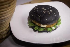 Close up photo of the opened black burger on a white plate is highly suitable for a fast food menu