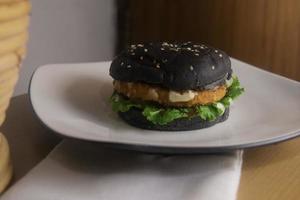 BLACK BURGER ON WHITE PLATE FROM FRONT ANGLE PHOTOGRAPHY photo