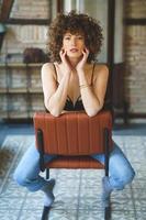 Seductive curly haired woman in bra sitting on chair in room photo