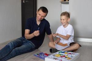 un linda chico en un blanco camiseta recoge un eléctrico diseñador con su papá en el habitación foto