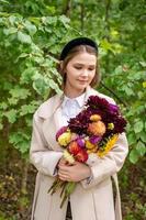 un linda niña con un negro venda y largo pelo sostiene un ramo de flores de otoño flores foto