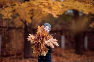 A cute boy in a hat holds autumn yellow leaves in his hands photo