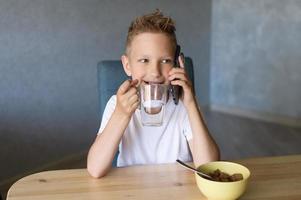 A cute boy drinks water and talks on the phone. Breakfast photo