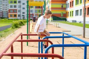 un Adolescente chico es comprometido en horizontal barras cerca el colegio foto