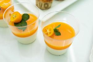 Mandarina panna cotta decorado con naranja china y menta en un el plastico vaso. postre para caramelo bar foto