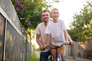 A cute boy in a white T-shirt rides a bike with his dad and laughs. photo