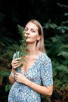 A girl in a dress holds a fern branch in her hands and looks at the camera photo