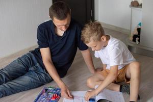 A cute boy in a white T-shirt collects an electrical designer with his dad in the room photo