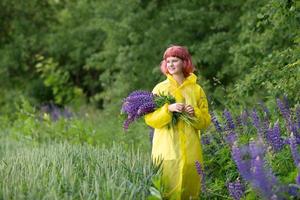 un linda Adolescente niña con rosado pelo y un ramo de flores de altramuces es en pie en un amarillo impermeable foto