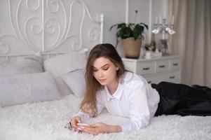 un joven negocio mujer es acostado en su cama y leyendo el Noticias o enviando un texto mensaje. foto