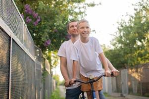 A cute boy in a white T-shirt rides a bike with his dad and laughs. photo