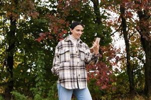 linda niña tiene un vídeo llamada en el teléfono en contra el antecedentes de un otoño bosque foto