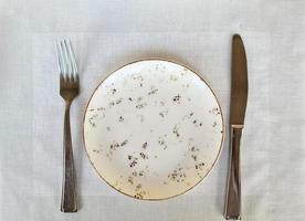 An empty light-coloured plate with knife and fork - view from above photo