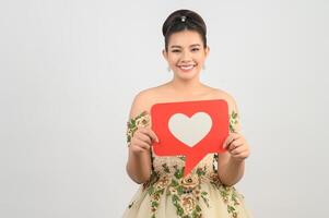 hermosa novia asiática sonriendo y posando con el signo del corazón en el fondo blanco foto