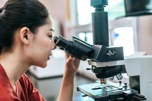 Asian young female farmer looking through a microscope in a laboratory. Modern technologies in agriculture management, agribusiness and research concept. photo