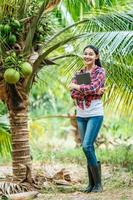 Portrait of Happy Asian young  farmer woman check quality of coconut in farm and using tablet computer to take orders online for customers. Agricultural and technology concepts. photo