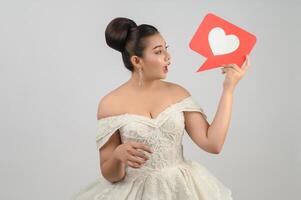 Asian beautiful bride smiling and posing with heart sign on white background photo