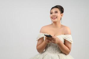 joven novia asiática hermosa que publica con un teléfono inteligente en la mano foto