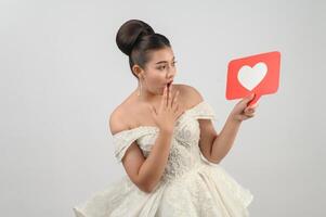 hermosa novia asiática sonriendo y posando con el signo del corazón en el fondo blanco foto