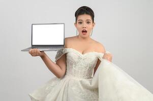 Young asian beautiful bride pose with mockup laptop computer in hand photo