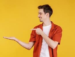 Portrait of happy smiling young man presenting and showing your text or product isolated on yellow background photo