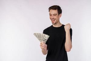 Portrait of a cheerful man holding dollar bills and doing winner gesture clenching fist over white background