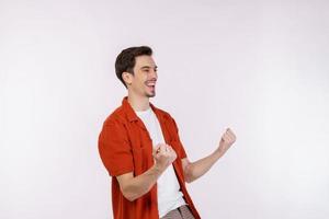 Portrait of happy joyful young man standing doing winner gesture clenching fists keeping isolated on white color wall background studio